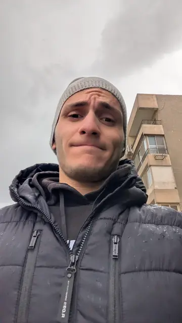 A selfie in a beanie and puffer jacket under a grey sky.