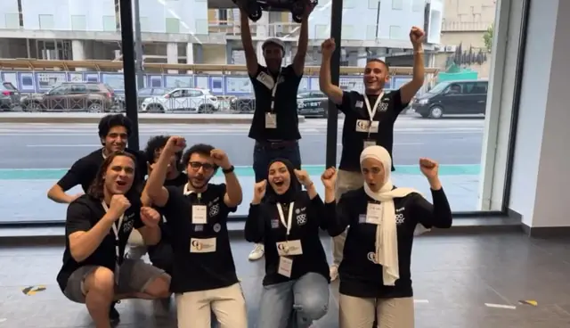 The team cheering with fists in the air, one teammate holding the car above his head.