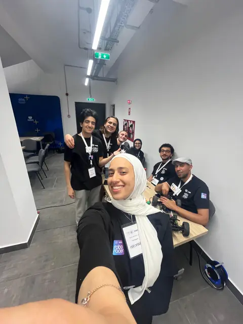 The team at a long table with the car, in Roboracer shirts and lanyards.