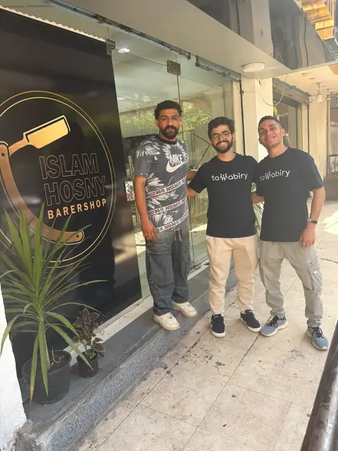 Three people outside a barbershop with a gold razor logo.