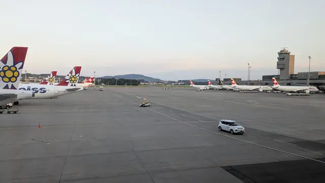 Airliners with red tails parked at Zurich, with the control tower behind.
